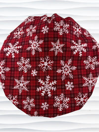 Red plaid bouffant scrub cap by jenscaps with white snowflake patterns displayed on a white mannequin head against a wavy white background.