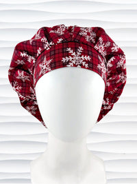 Red plaid bouffant scrub cap by jenscaps with white snowflake patterns displayed on a white mannequin head against a wavy white background.