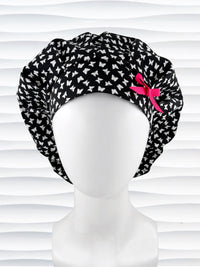 Bouffant surgical scrub cap by JensCaps with white butterflies all over black cotton fabric and shown with a hot pink bow on the front