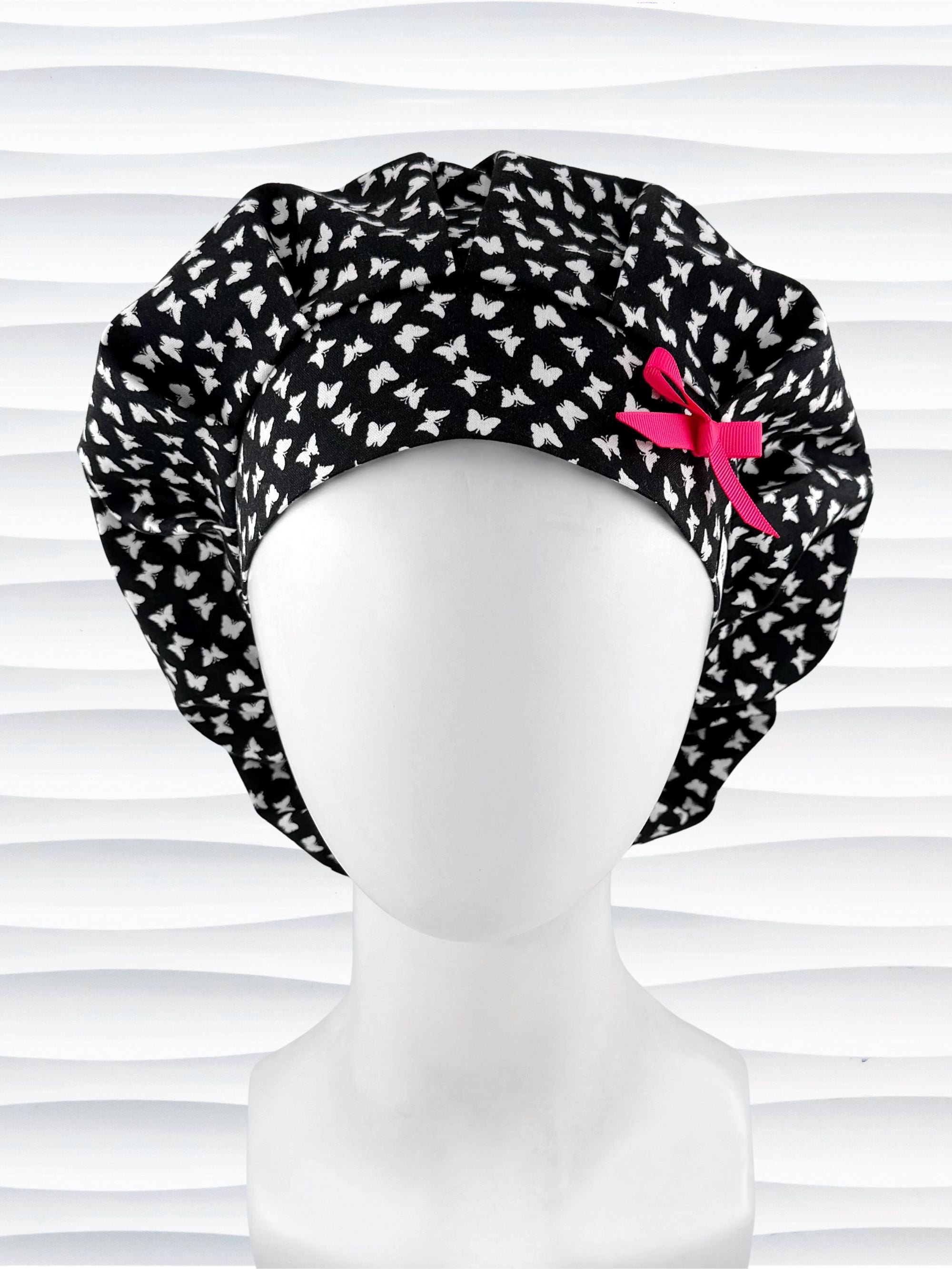 Bouffant surgical scrub cap by JensCaps with white butterflies all over black cotton fabric and shown with a hot pink bow on the front