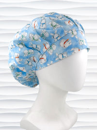 Bouffant style surgical scrub cap by JensCaps with white bunnies wearing beanies and scarves tossed all over this light blue cotton fabric and displayed on a white mannequin head