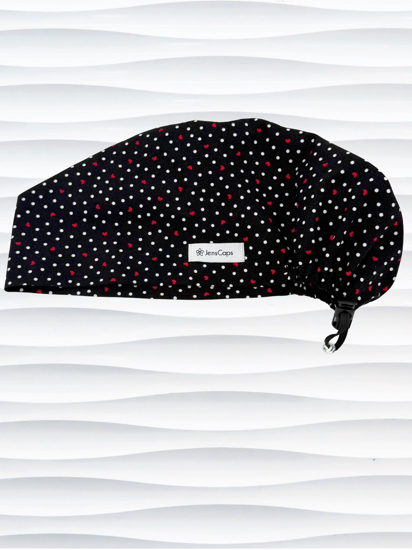 Euro Pixie surgical scrub cap by JensCaps with small red hearts and white dots all over this black cotton fabric and displayed on a white mannequin head.