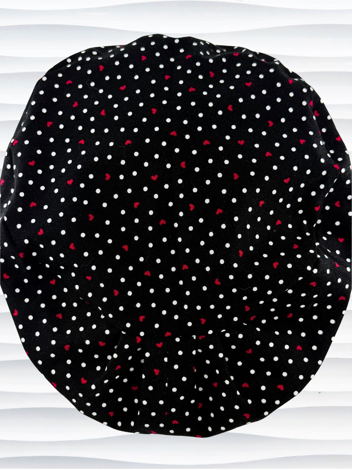 Euro Pixie surgical scrub cap by JensCaps with small red hearts and white dots all over this black cotton fabric and displayed on a white mannequin head.