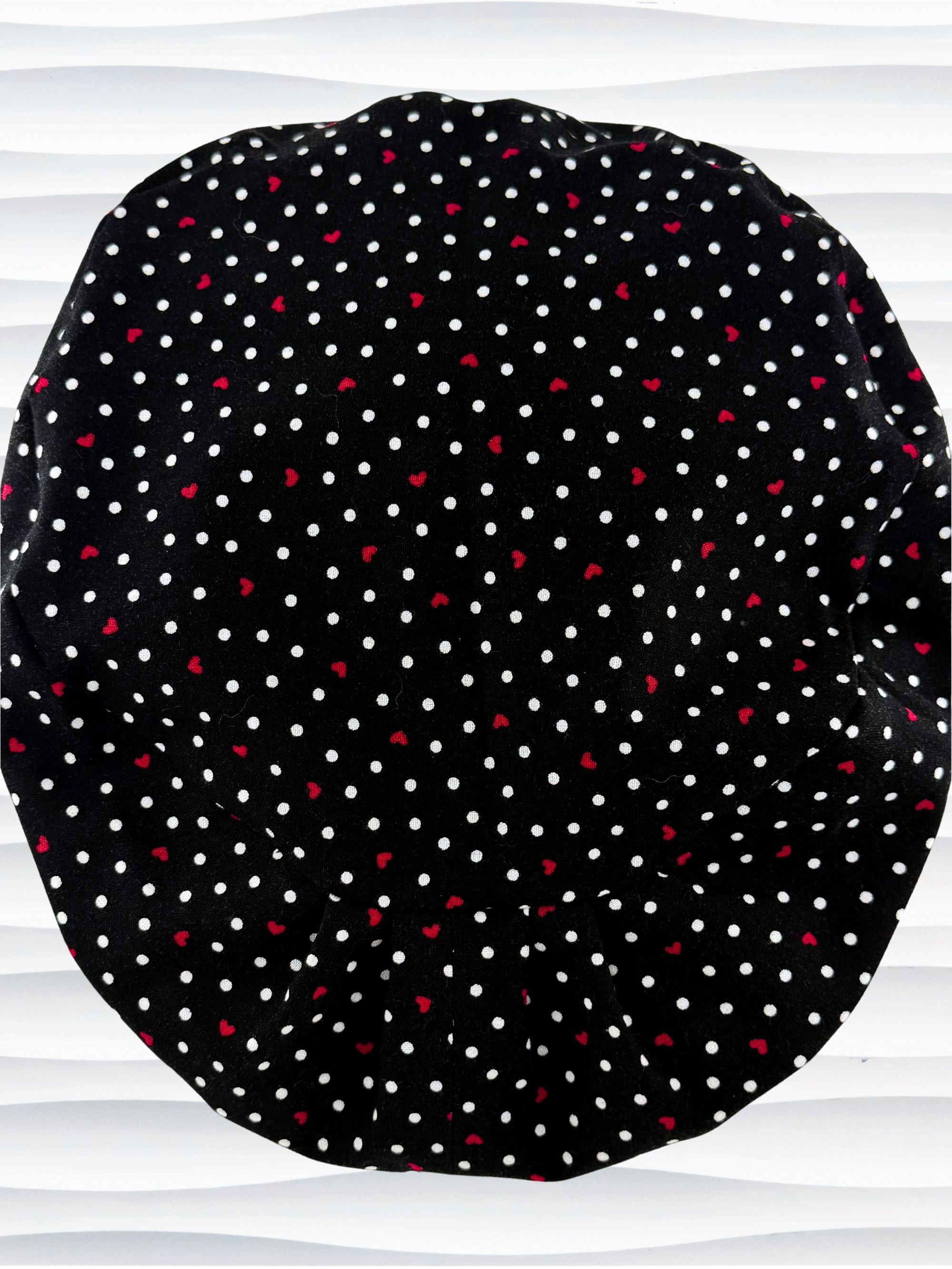 Euro Pixie surgical scrub cap by JensCaps with small red hearts and white dots all over this black cotton fabric and displayed on a white mannequin head.