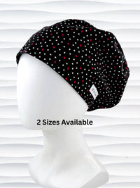 Euro Pixie surgical scrub cap by JensCaps with small red hearts and white dots all over this black cotton fabric and displayed on a white mannequin head.