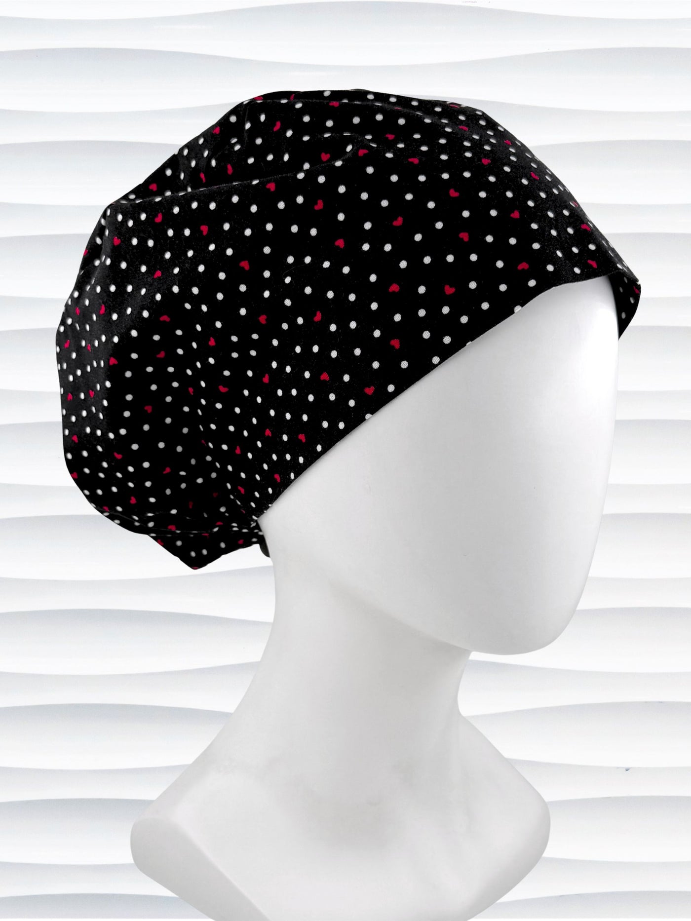 Euro Pixie surgical scrub cap by JensCaps with small red hearts and white dots all over this black cotton fabric and displayed on a white mannequin head.