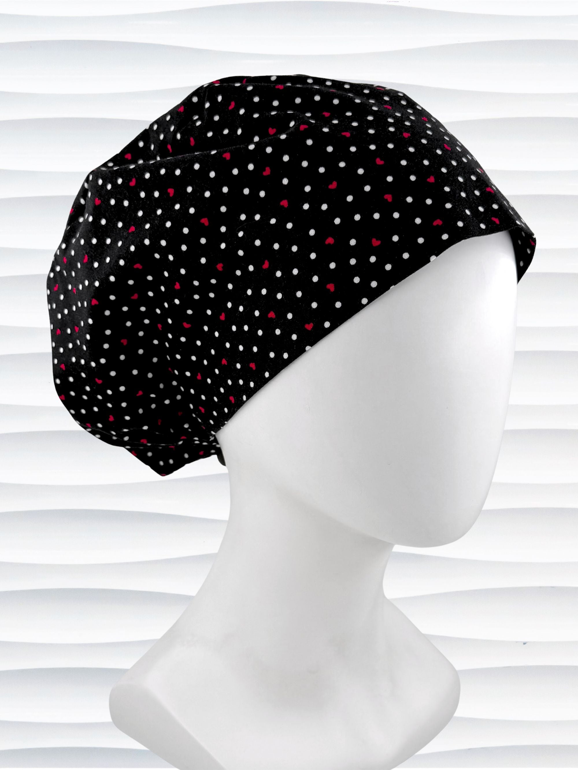 Euro Pixie surgical scrub cap by JensCaps with small red hearts and white dots all over this black cotton fabric and displayed on a white mannequin head.