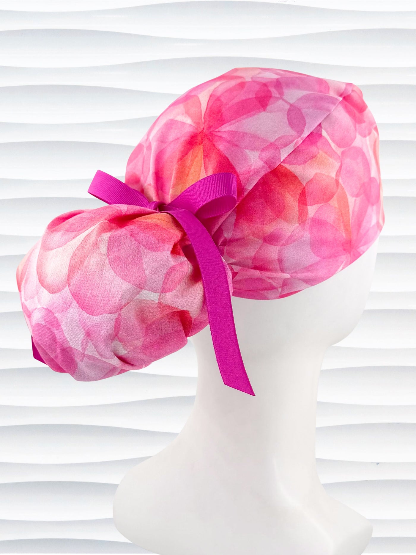 Ponytail  style surgical scrub cap by JensCaps with large flowers in light and dark pinks and peach sorbet on cotton fabric, finished with a ribbon tie, and displayed on a white mannequin head.