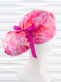 Ponytail  style surgical scrub cap by JensCaps with large flowers in light and dark pinks and peach sorbet on cotton fabric, finished with a ribbon tie, and displayed on a white mannequin head.