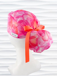 Pink floral-patterned scrub cap with an orange bow on a white mannequin head against a white background