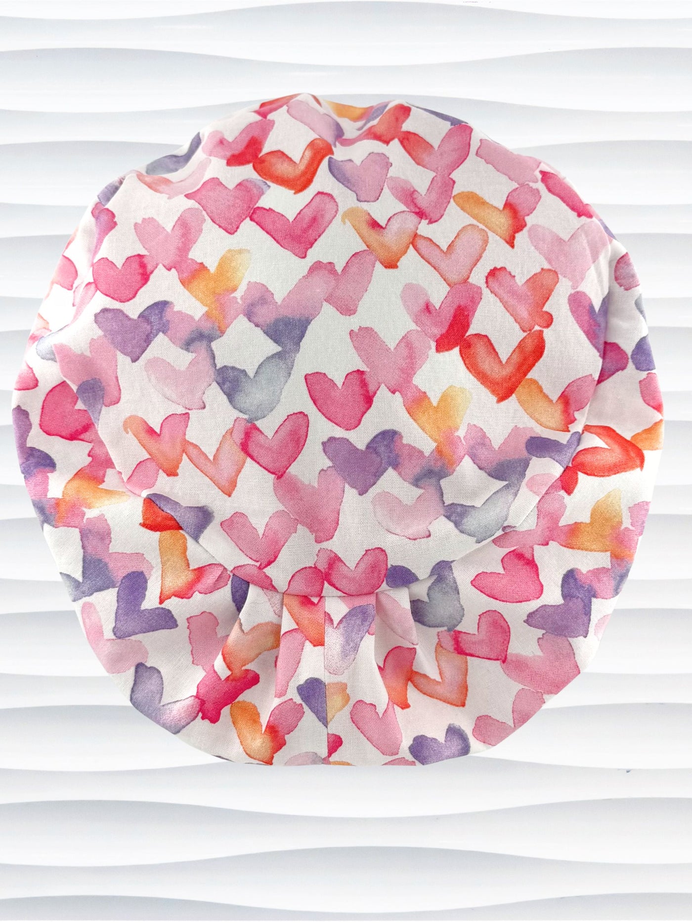 Euro Pixie style surgical scrub cap by JensCaps with watercolor hearts in pastel colors all over white cotton fabric and is displayed on a white mannequin head.