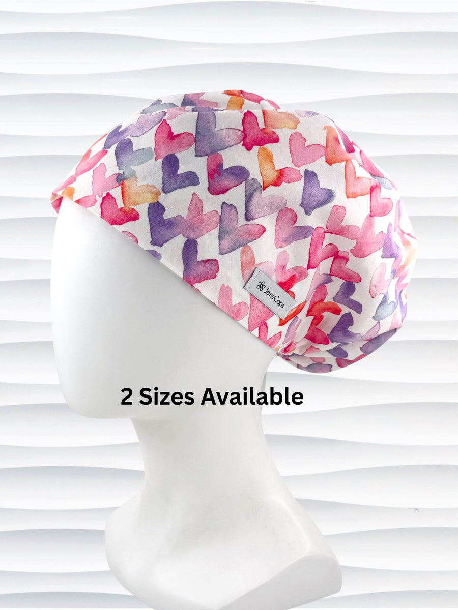 Euro Pixie style surgical scrub cap by JensCaps with watercolor hearts in pastel colors all over white cotton fabric and is displayed on a white mannequin head.