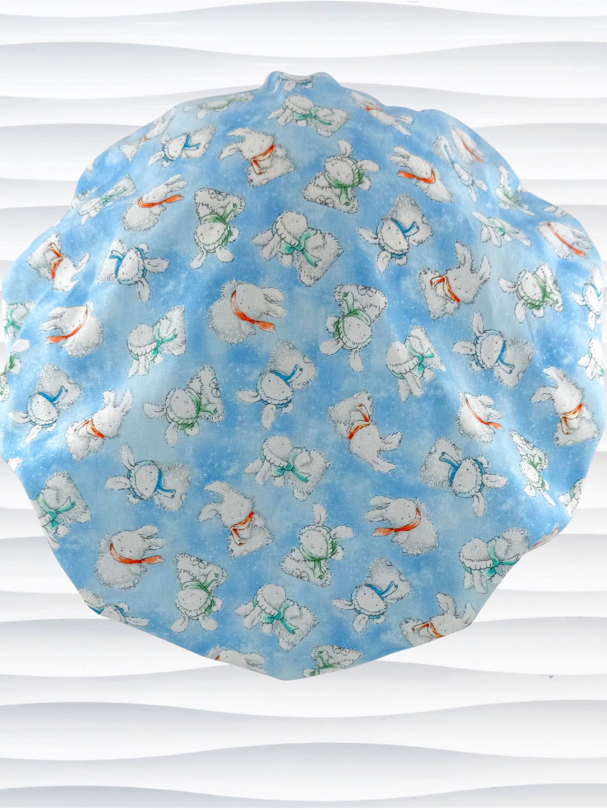 Bouffant style surgical scrub cap by JensCaps with white bunnies wearing beanies and scarves tossed all over this light blue cotton fabric and displayed on a white mannequin head