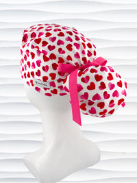 Ponytail style surgical scrub cap by JensCaps with pink to red ombre hearts all over a white background, finished with a ribbon tie, and displayed on a white mannequin head
