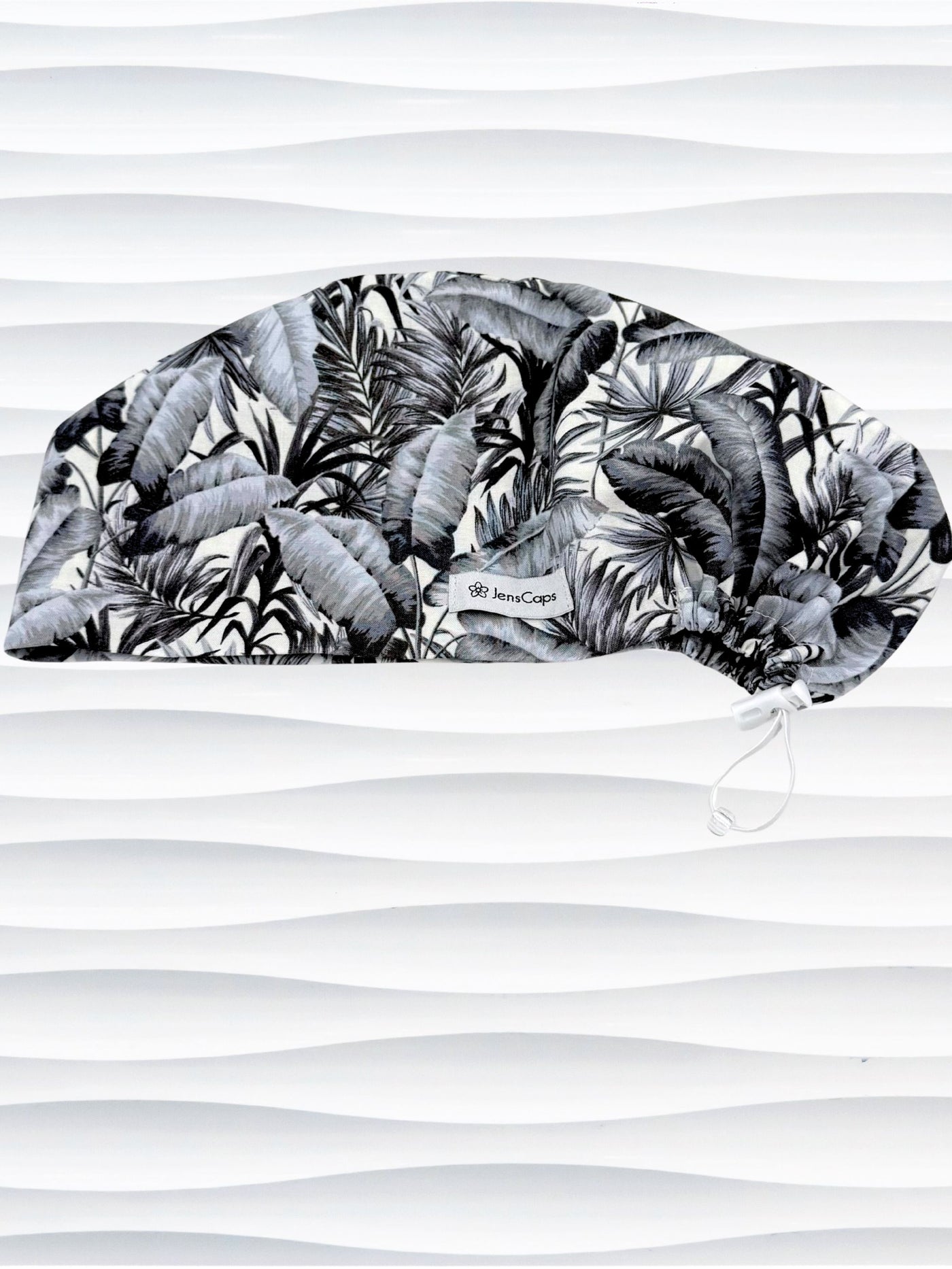 Euro Pixie style surgial scrub cap by JensCaps with black and white palm trees and banana palm leaves displayed on a mannequin head