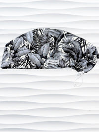 Euro Pixie style surgial scrub cap by JensCaps with black and white palm trees and banana palm leaves displayed on a mannequin head