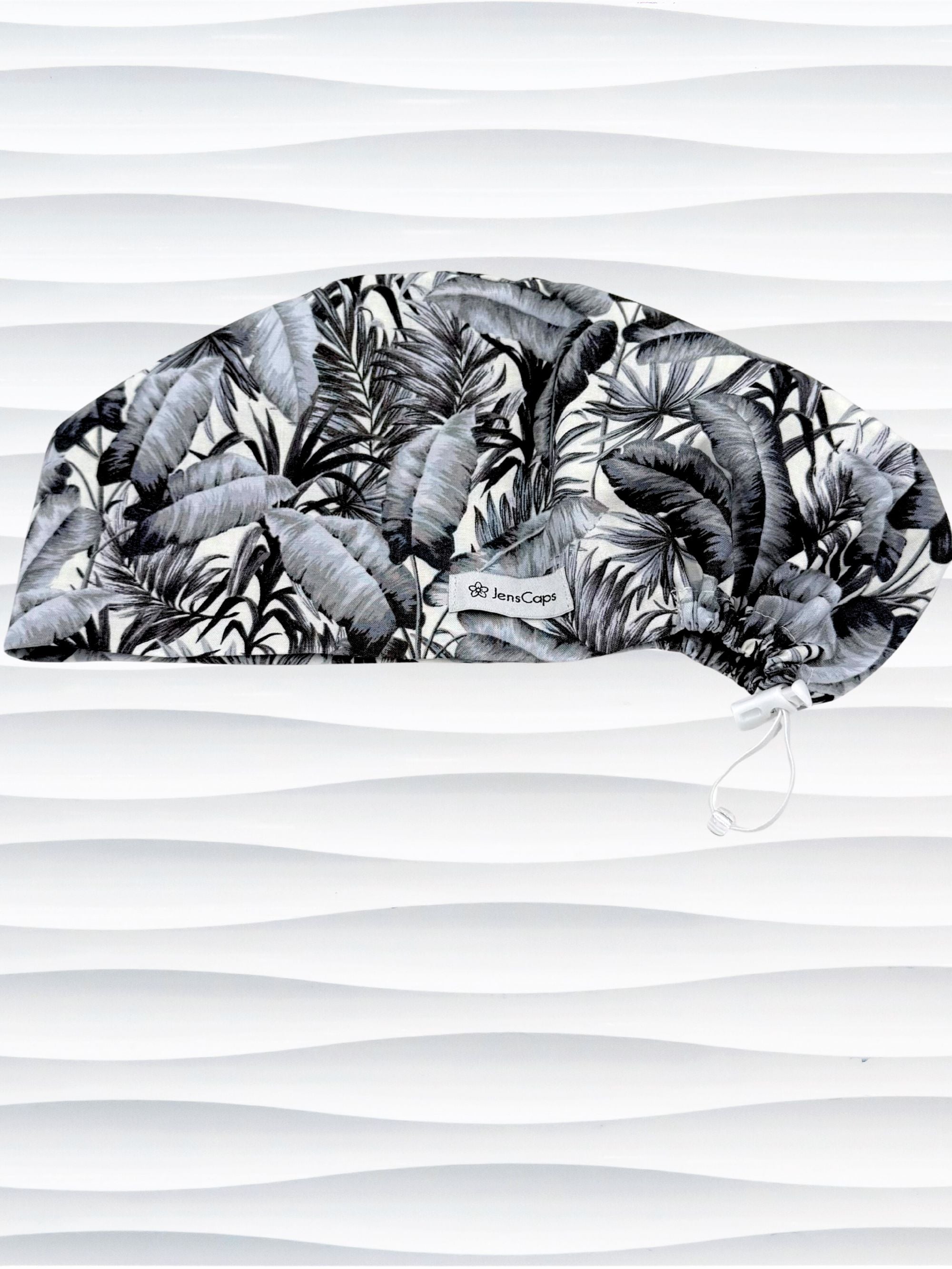 Euro Pixie style surgial scrub cap by JensCaps with black and white palm trees and banana palm leaves displayed on a mannequin head
