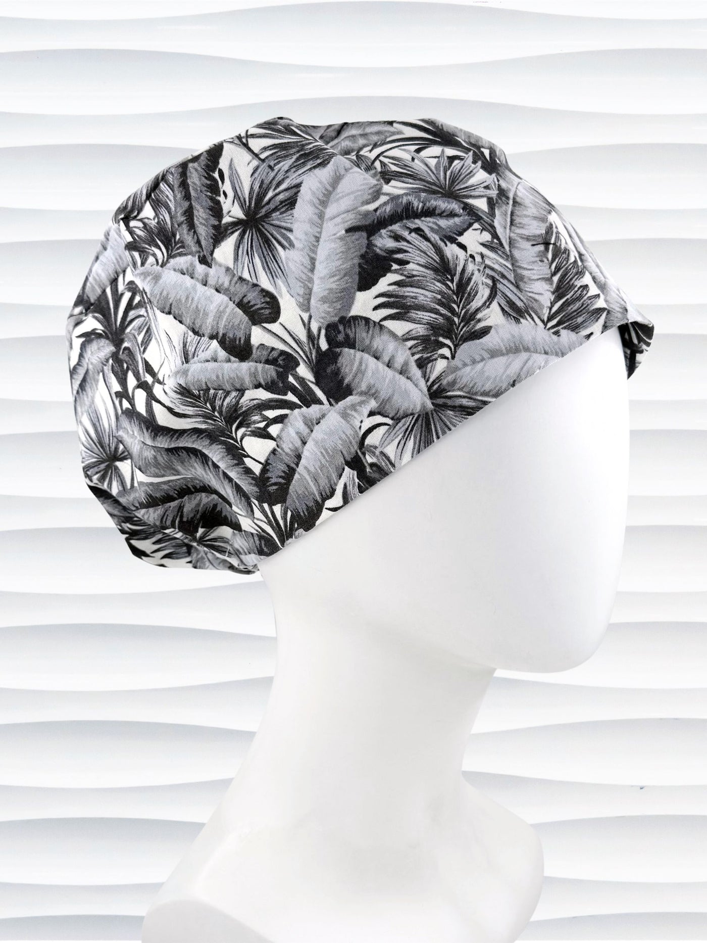 Euro Pixie style surgial scrub cap by JensCaps with black and white palm trees and banana palm leaves displayed on a mannequin head