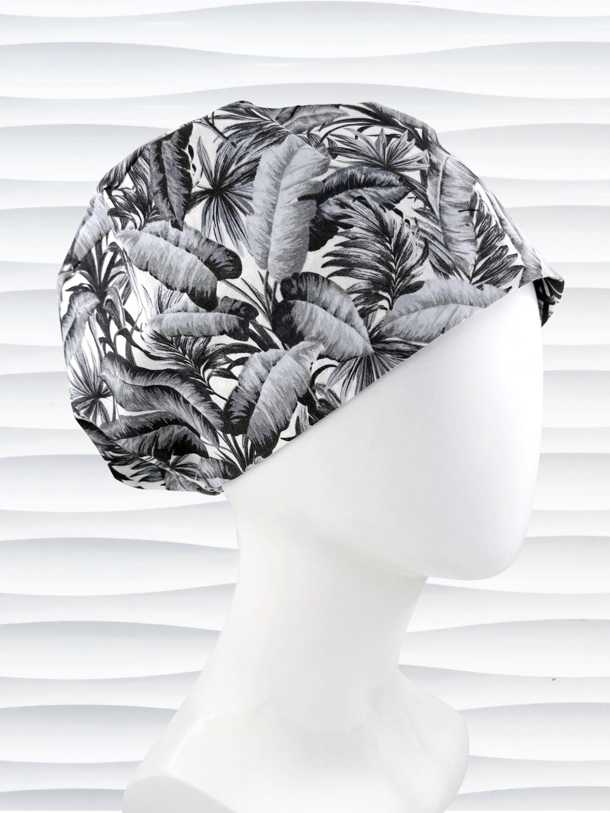 Euro Pixie style surgial scrub cap by JensCaps with black and white palm trees and banana palm leaves displayed on a mannequin head