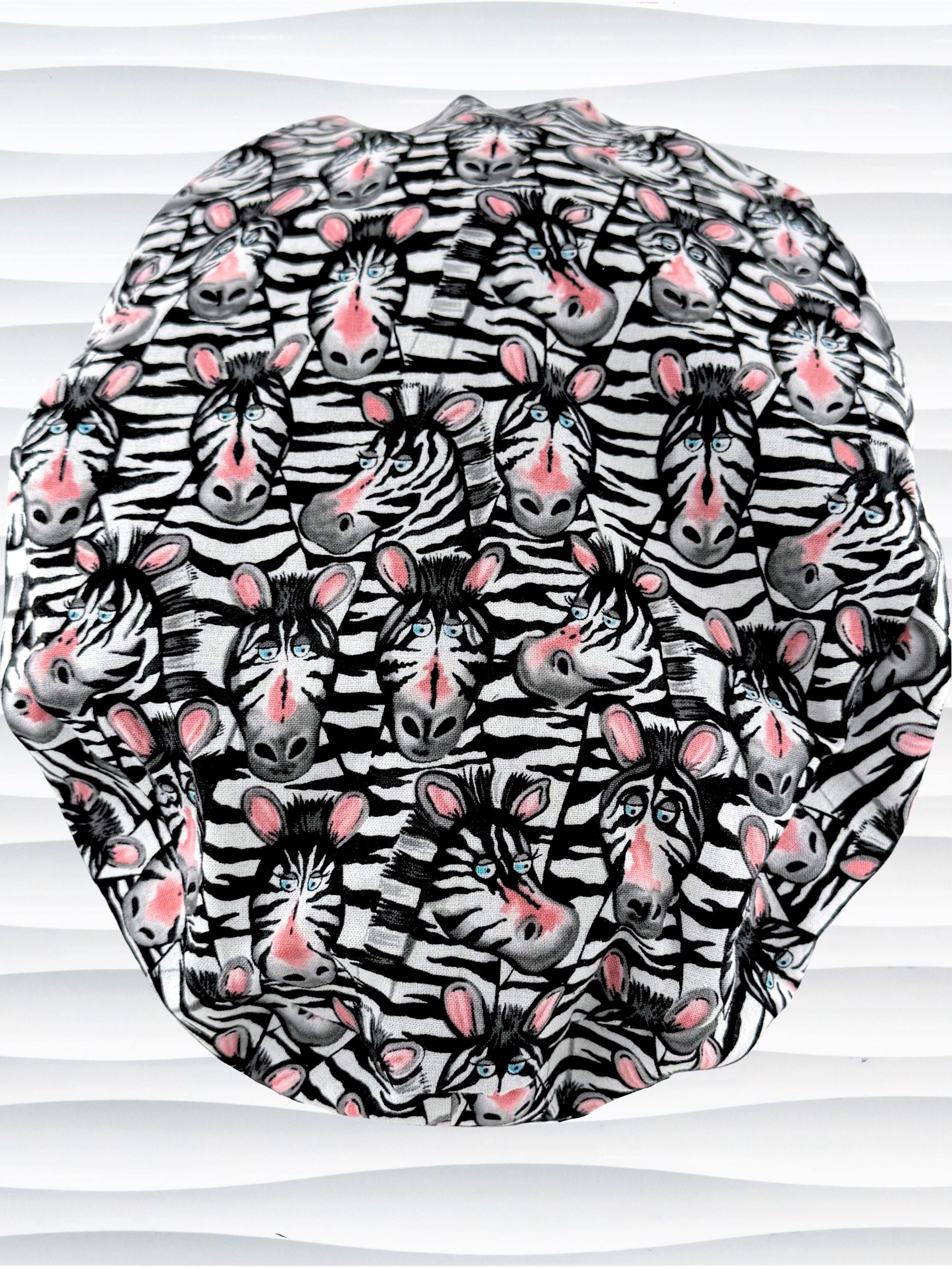Euro ponytail style surgical scrub cap featuring a black and white zebra print with blue eyes and pink accents with an adjustable back tie and displayed on a mannequin head