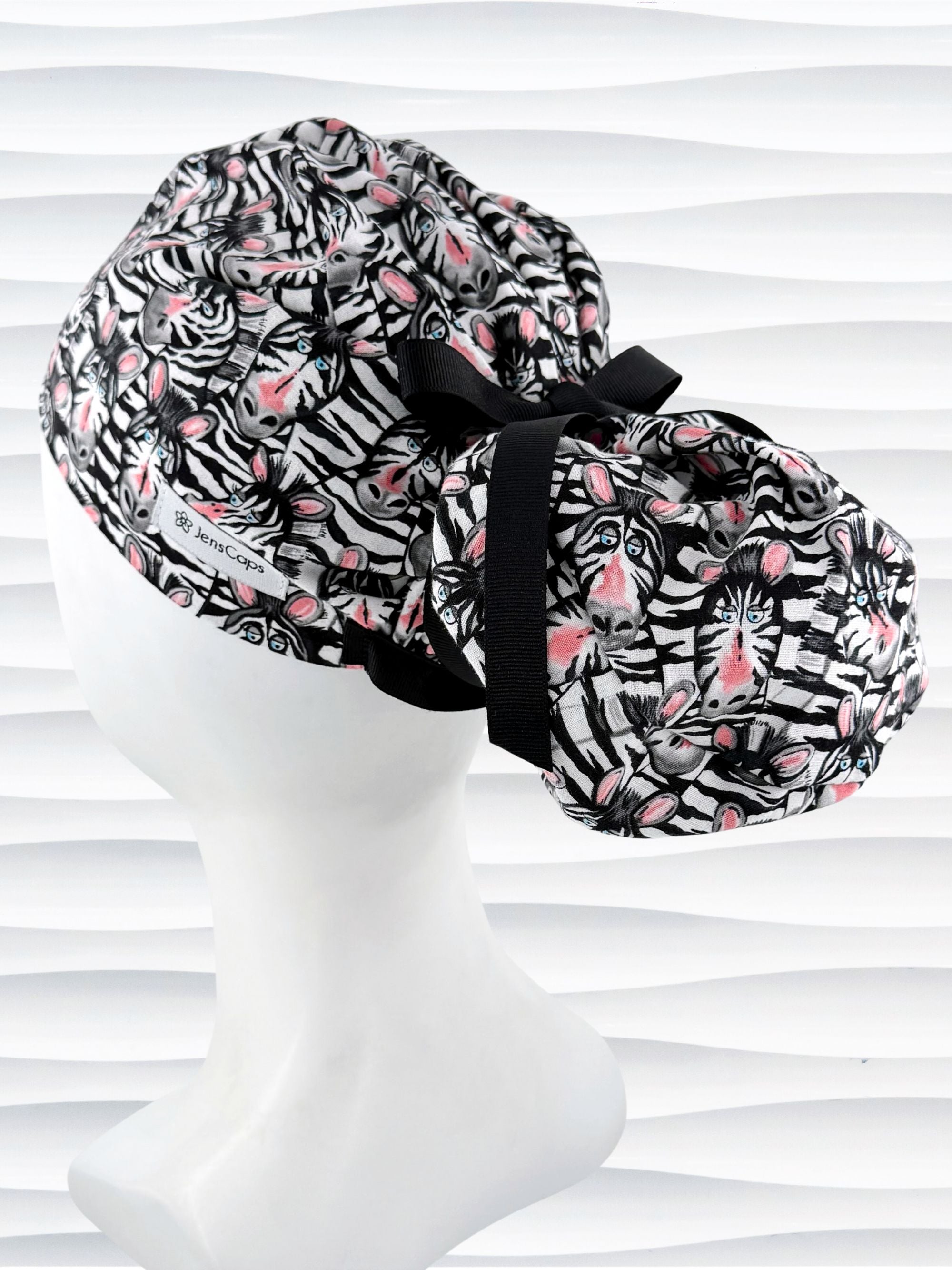 Euro ponytail style surgical scrub cap featuring a black and white zebra print with blue eyes and pink accents with an adjustable back tie and displayed on a mannequin head