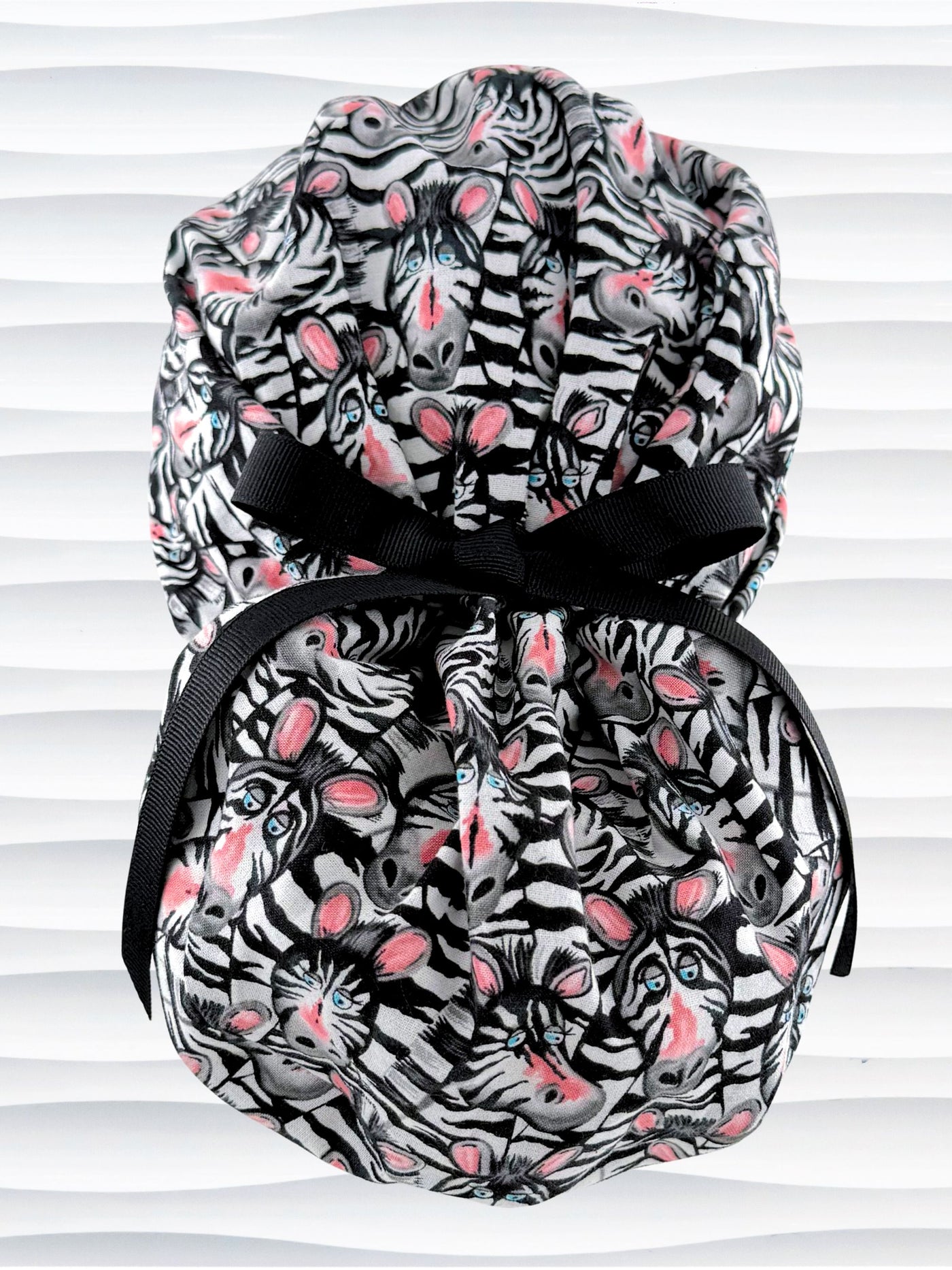 Euro ponytail style surgical scrub cap featuring a black and white zebra print with blue eyes and pink accents with an adjustable back tie and displayed on a mannequin head