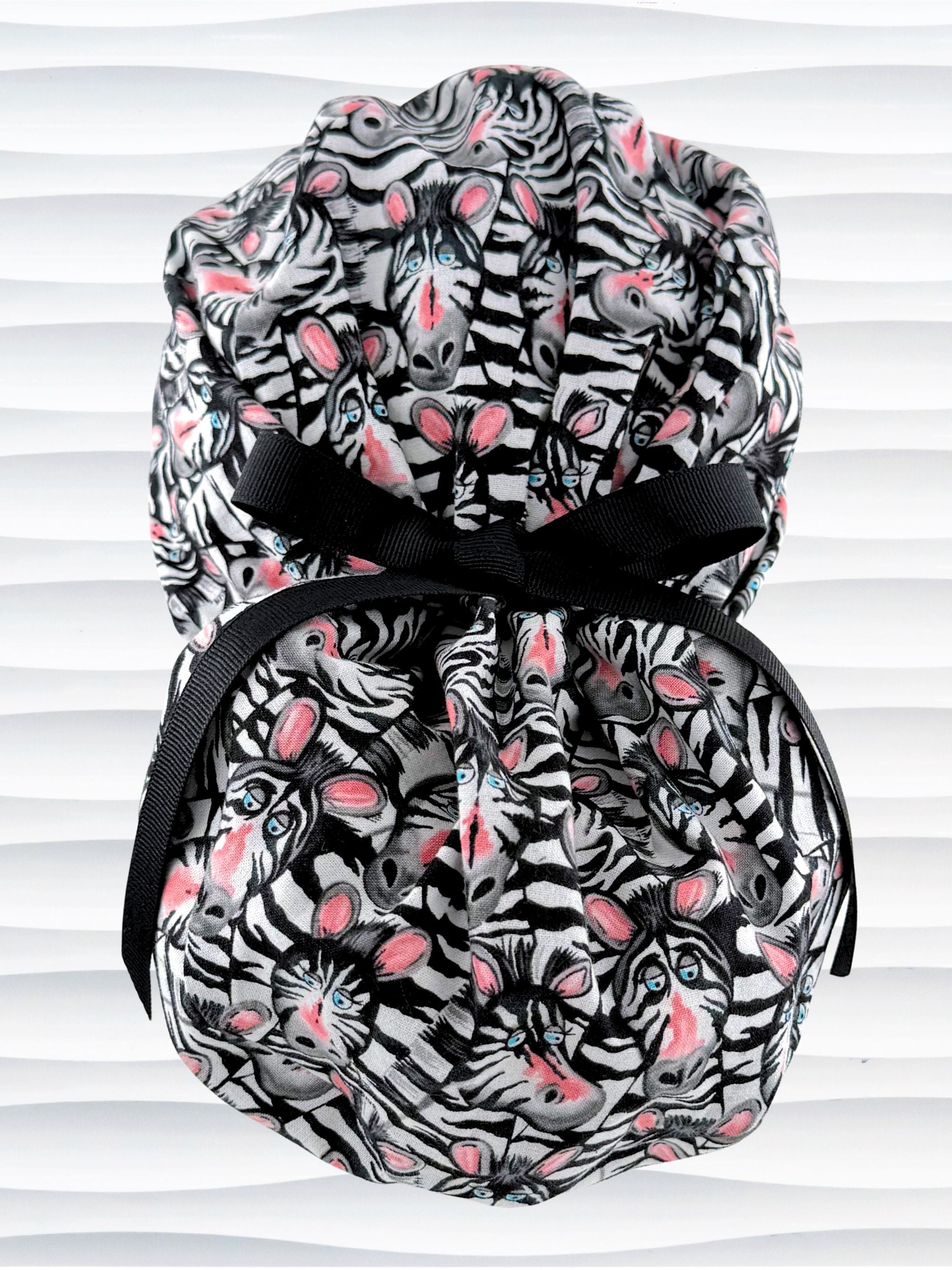 Euro ponytail style surgical scrub cap featuring a black and white zebra print with blue eyes and pink accents with an adjustable back tie and displayed on a mannequin head