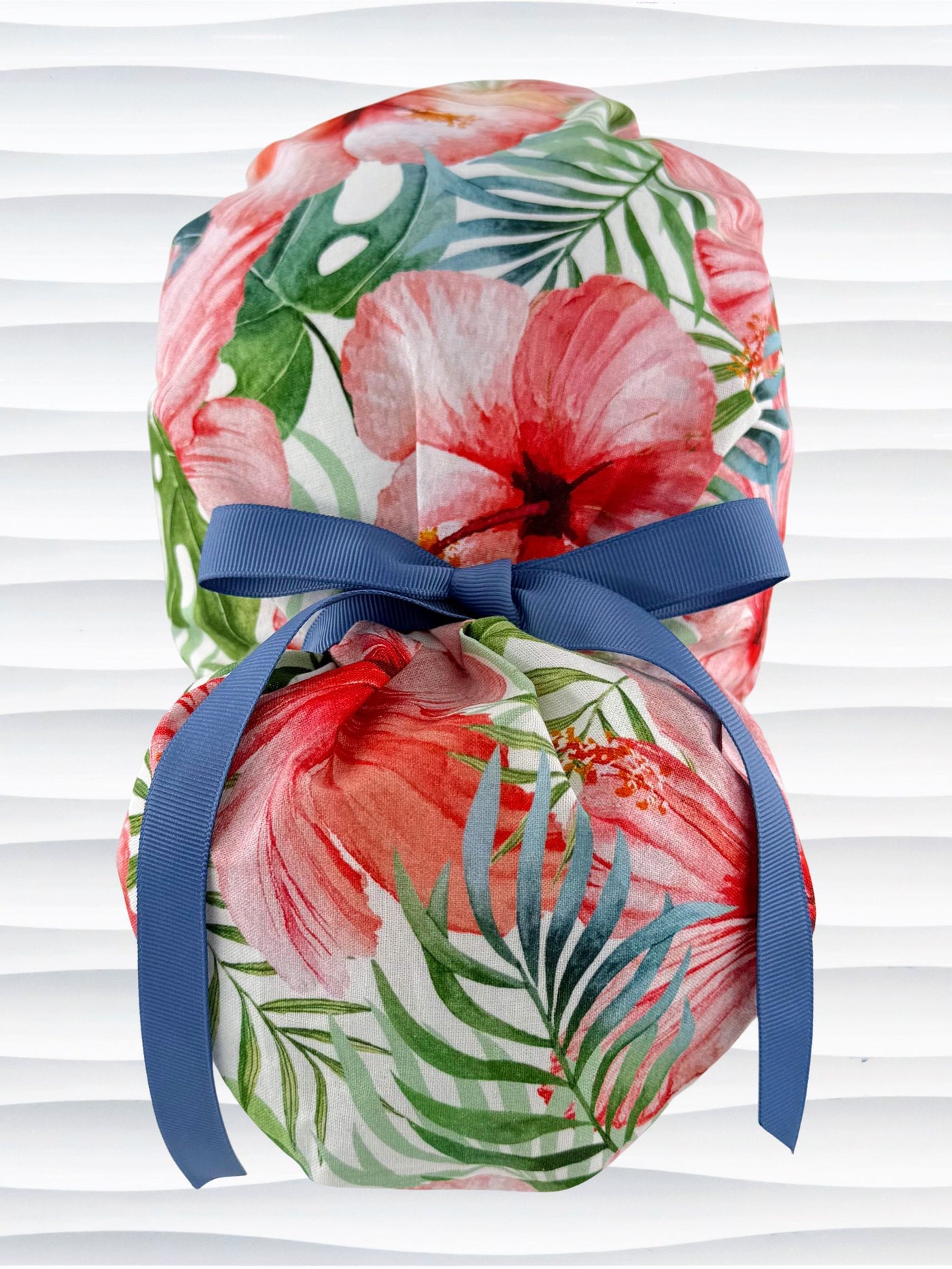 Ponytail style surgical scrub cap by JensCaps with tropical hibiscus flowers and palm fronds all over white cotton fabric, finished with a grosgrain ribbon tie, and displayed on a mannequin head