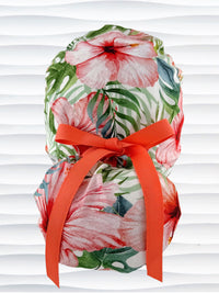 Ponytail style surgical scrub cap by JensCaps with tropical hibiscus flowers and palm fronds all over white cotton fabric, finished with a grosgrain ribbon tie, and displayed on a mannequin head