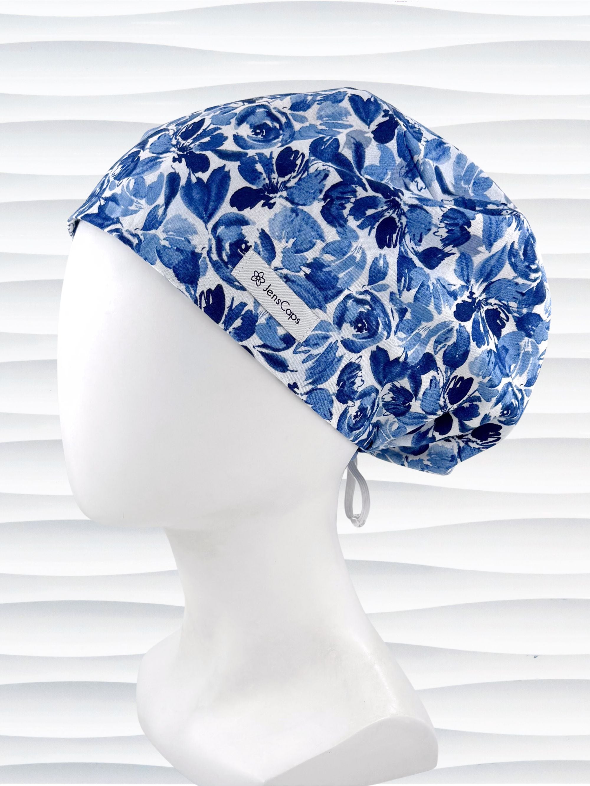 Euro Pixie style surgical scrub cap by JensCaps with flowers in varying shades of blue with a white background displayed on a white mannequin head.