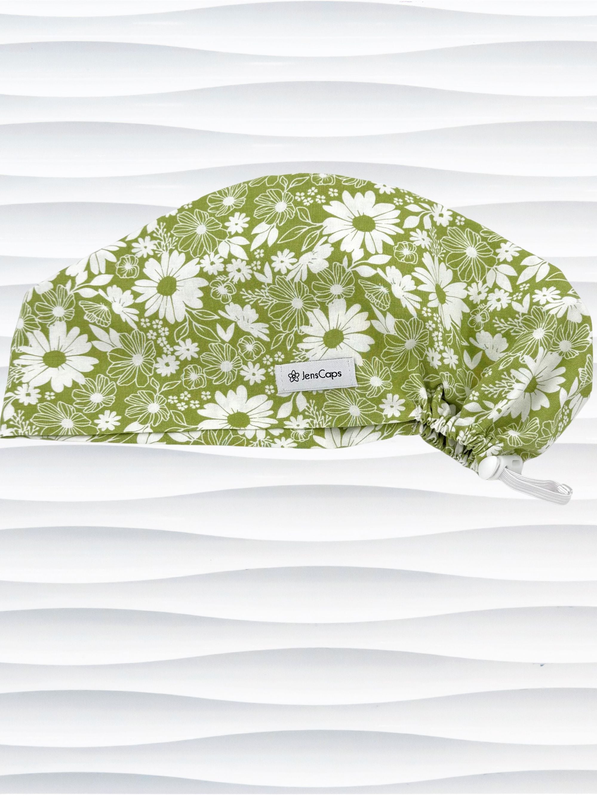 Euro Pixie style surgical scrub cap by JensCaps with white daisies and flowers all over a light green background cotton fabric and displayed on a mannequin head.