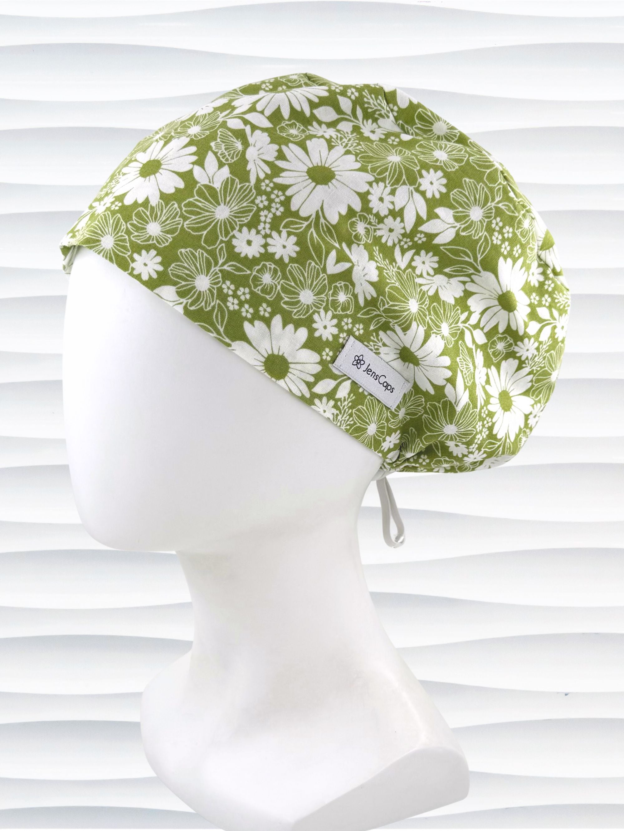 Euro Pixie style surgical scrub cap by JensCaps with white daisies and flowers all over a light green background cotton fabric and displayed on a mannequin head.