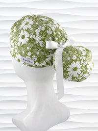 Ponytail style surgical scrub cap with white daisies and flowers all over a light green cotton fabric, finished with a grosgrain ribbon tie, and displayed on a mannequin head.