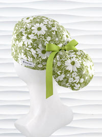 Ponytail style surgical scrub cap with white daisies and flowers all over a light green cotton fabric, finished with a grosgrain ribbon tie, and displayed on a mannequin head.