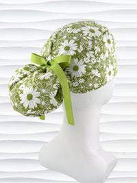 Ponytail style surgical scrub cap with white daisies and flowers all over a light green cotton fabric, finished with a grosgrain ribbon tie, and displayed on a mannequin head.