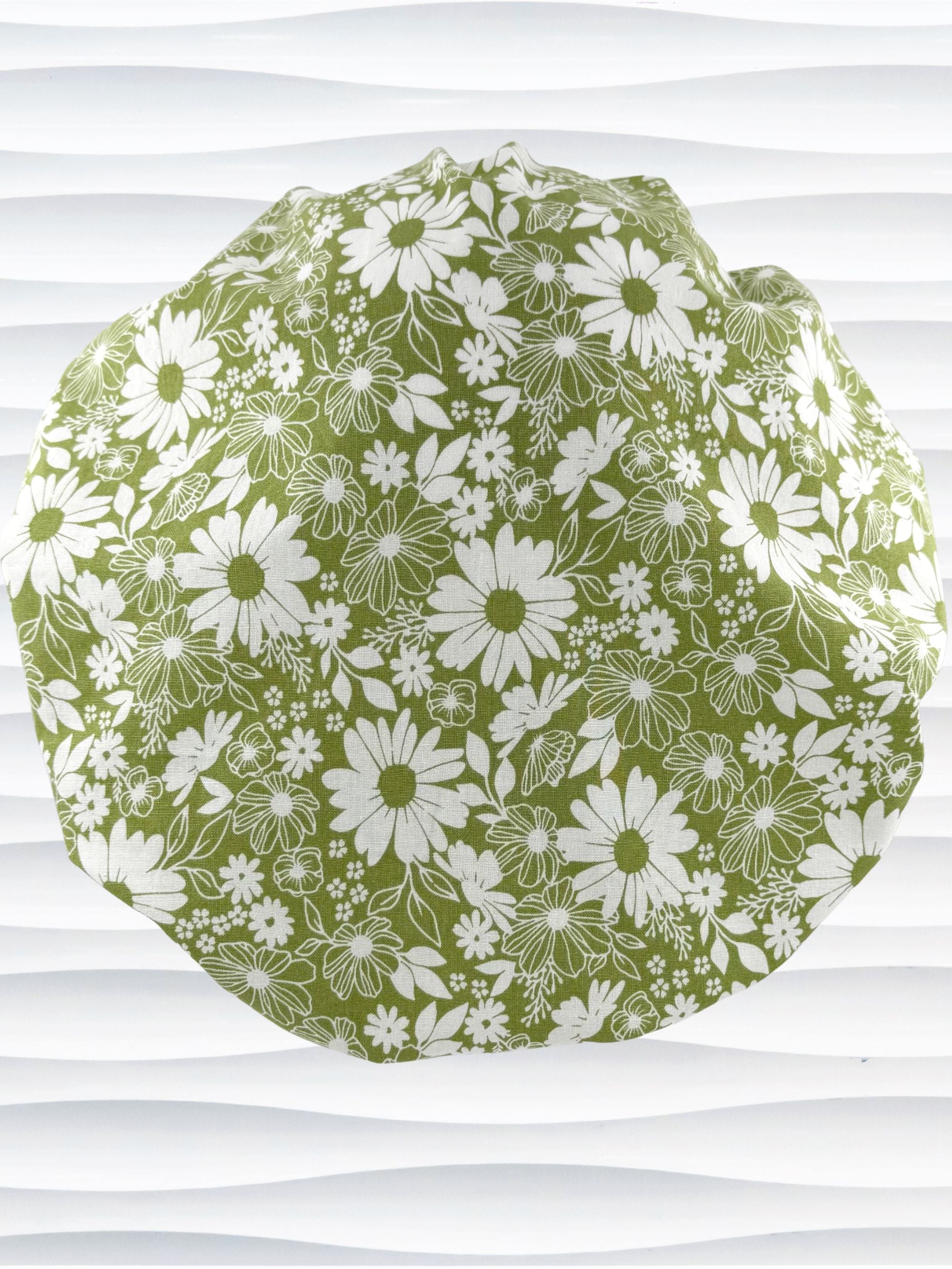 Bouffant style surgical scrub cap by JensCaps with white daisies and flowers all over a light green background cotton fabric and displayed on a mannequin head.
