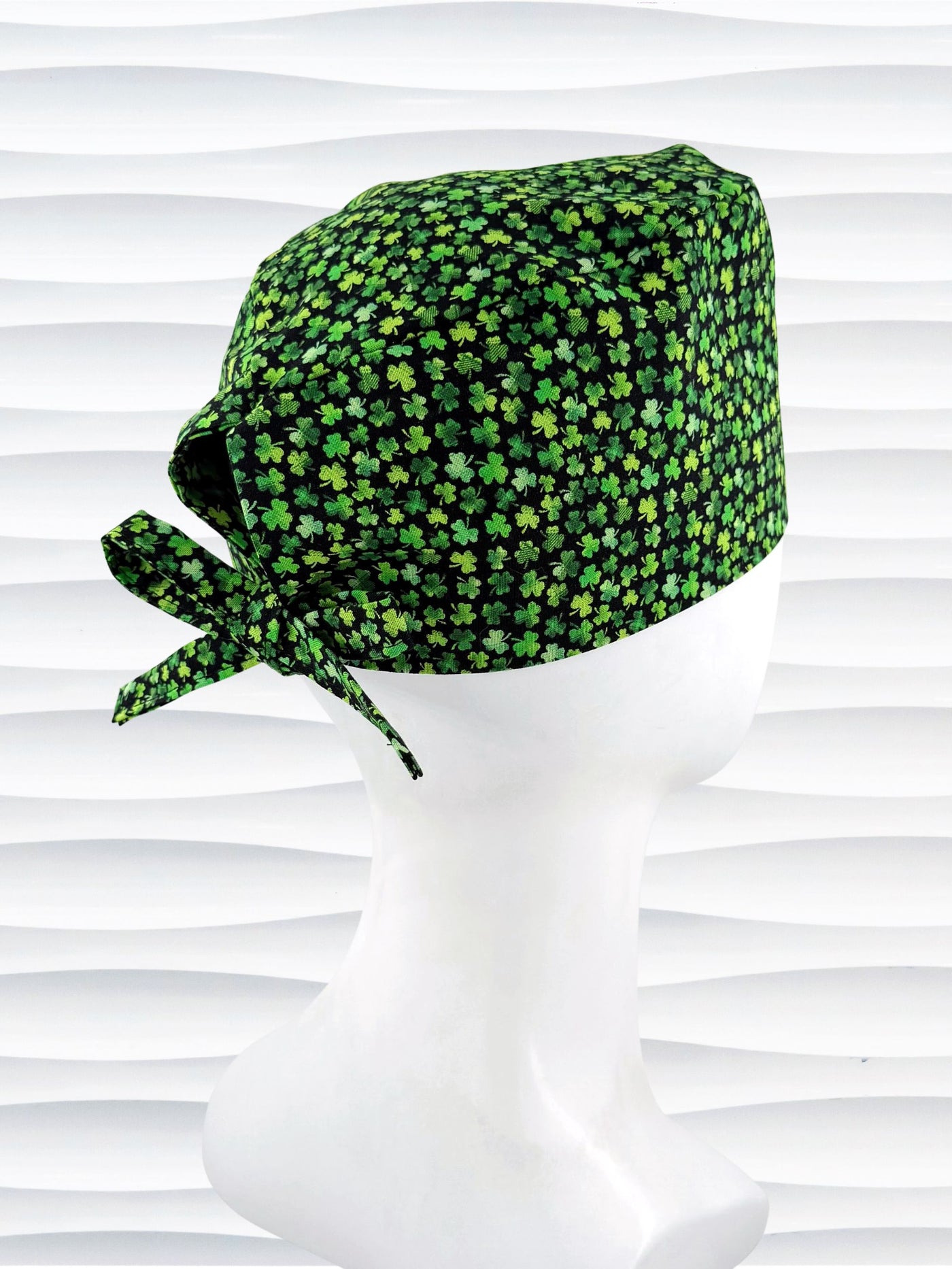 Mens style surgial scrub cap with small greencshamrocks on black cotton fabric and displayed on mannequin head.