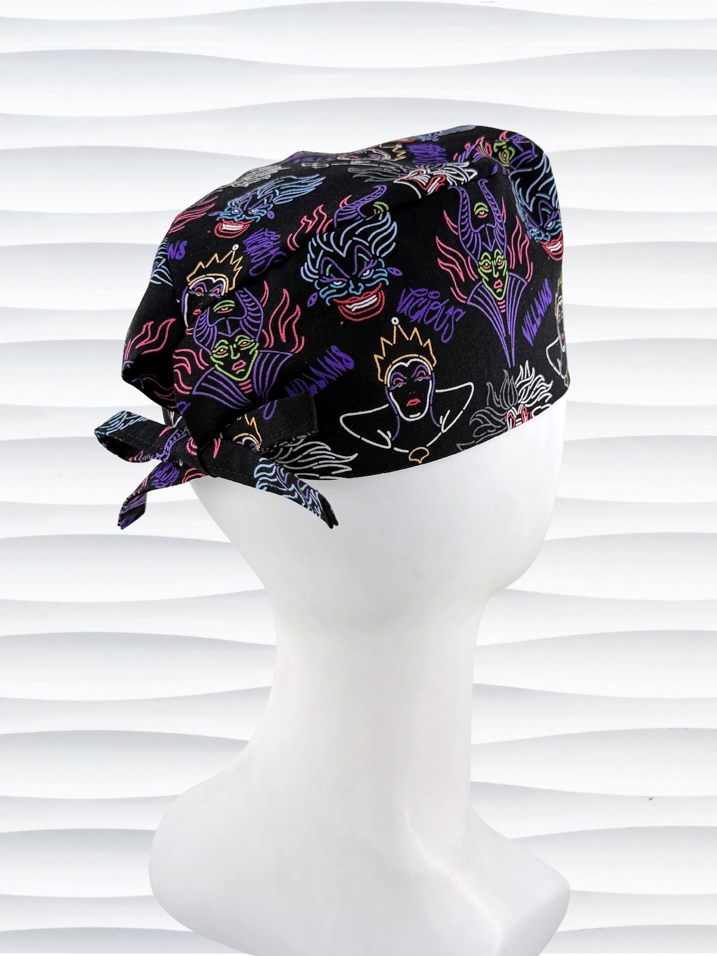 Mens style surgical scrub skull cap with neon colors of iconic villains and queens all over black cotton fabric and displayed on mannequin head.