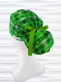 Green plaid ponytail style surgical scrub cap with shamrock pattern on a mannequin head against a white background