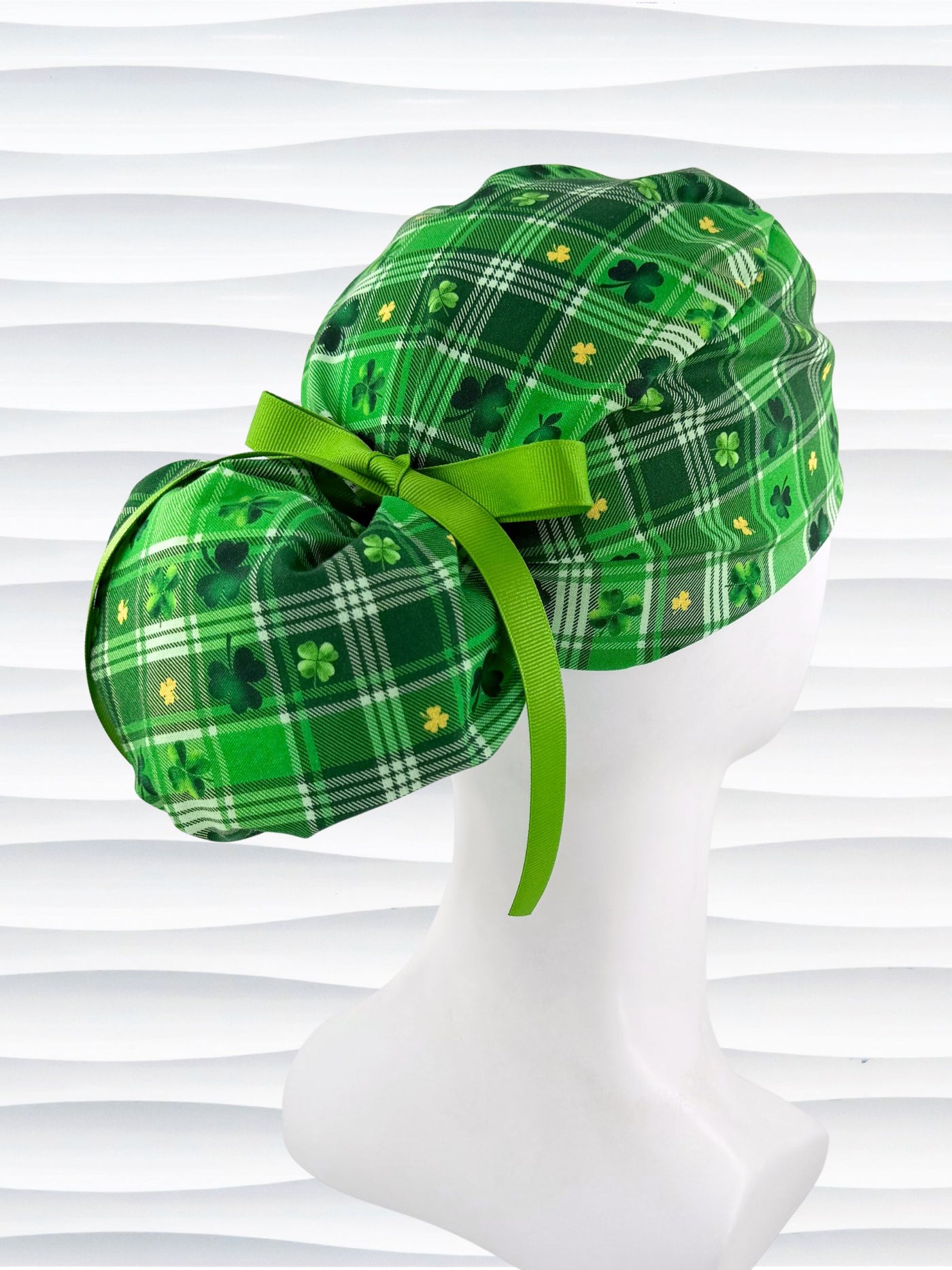 Green plaid ponytail style surgical scrub cap with shamrock pattern on a mannequin head against a white background