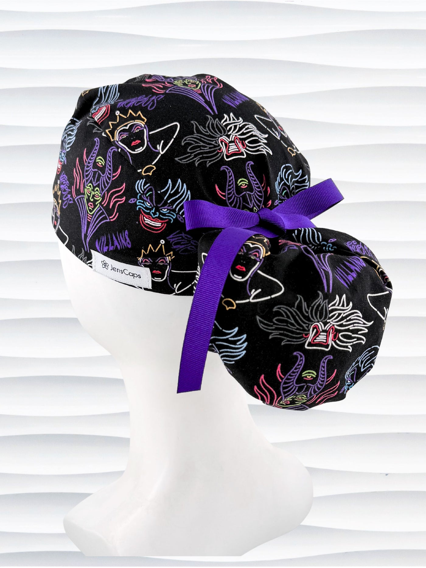 Ponytail style surgical scrub cap with neon colors of iconic villains all over black cotton fabric, finished with a ribbon tie and displayed on mannequin head.