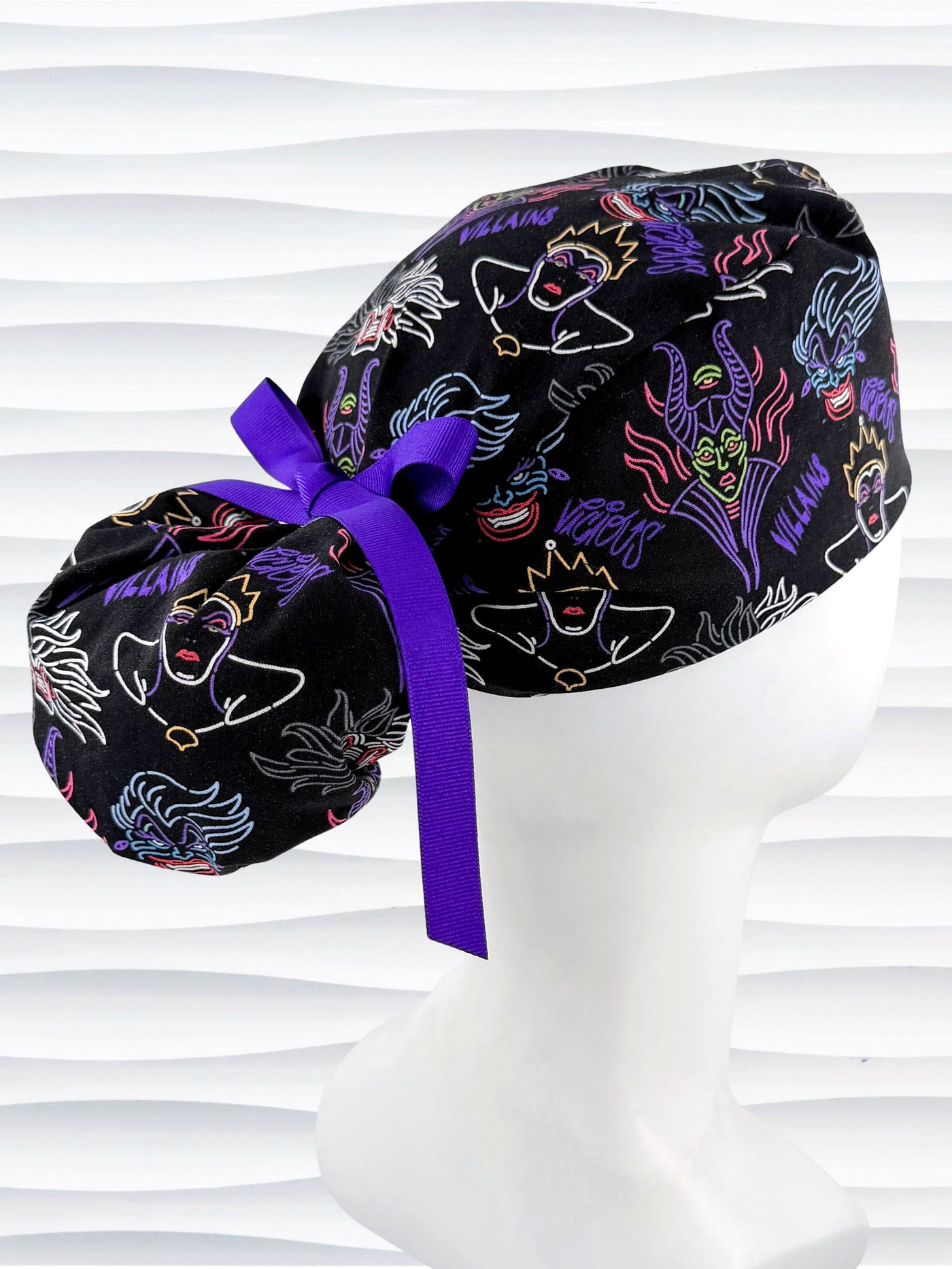 Ponytail style surgical scrub cap with neon colors of iconic villains all over black cotton fabric, finished with a ribbon tie and displayed on mannequin head.