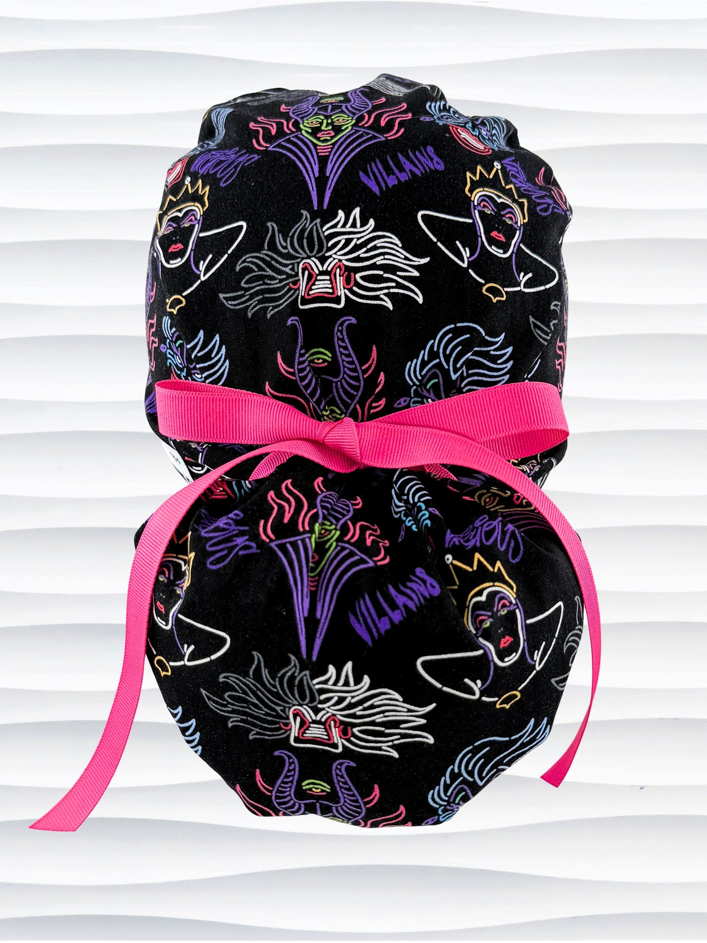 Ponytail style surgical scrub cap with neon colors of iconic villains all over black cotton fabric, finished with a ribbon tie and displayed on mannequin head.