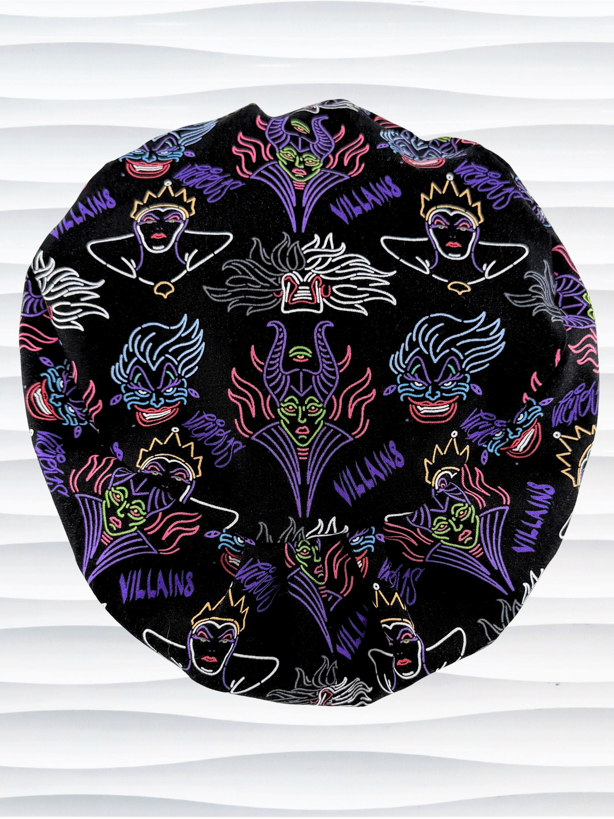 Euro Pixie style surgical scrub cap by JensCaps with neon colors of iconic villains all over black cotton fabric and displayed on mannequin head.