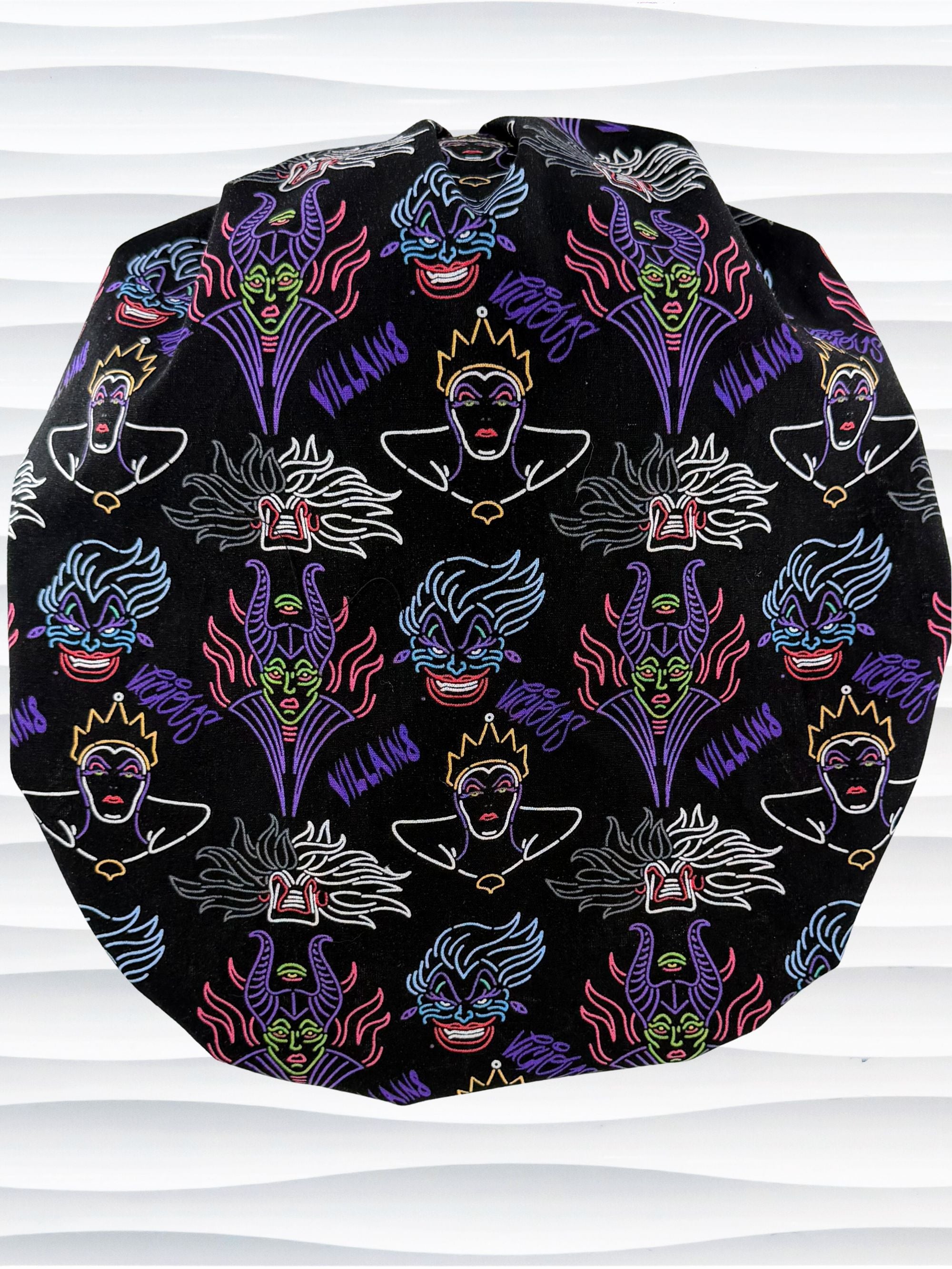 Bouffant style surgical scrub cap with neon colors of iconic villains all over black cotton fabric and displayed on mannequin head.