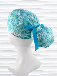 Ponytail style surgical scrub cap by JensCaps with abstract greens and blues on white cotton fabric and displayed on mannequin head.