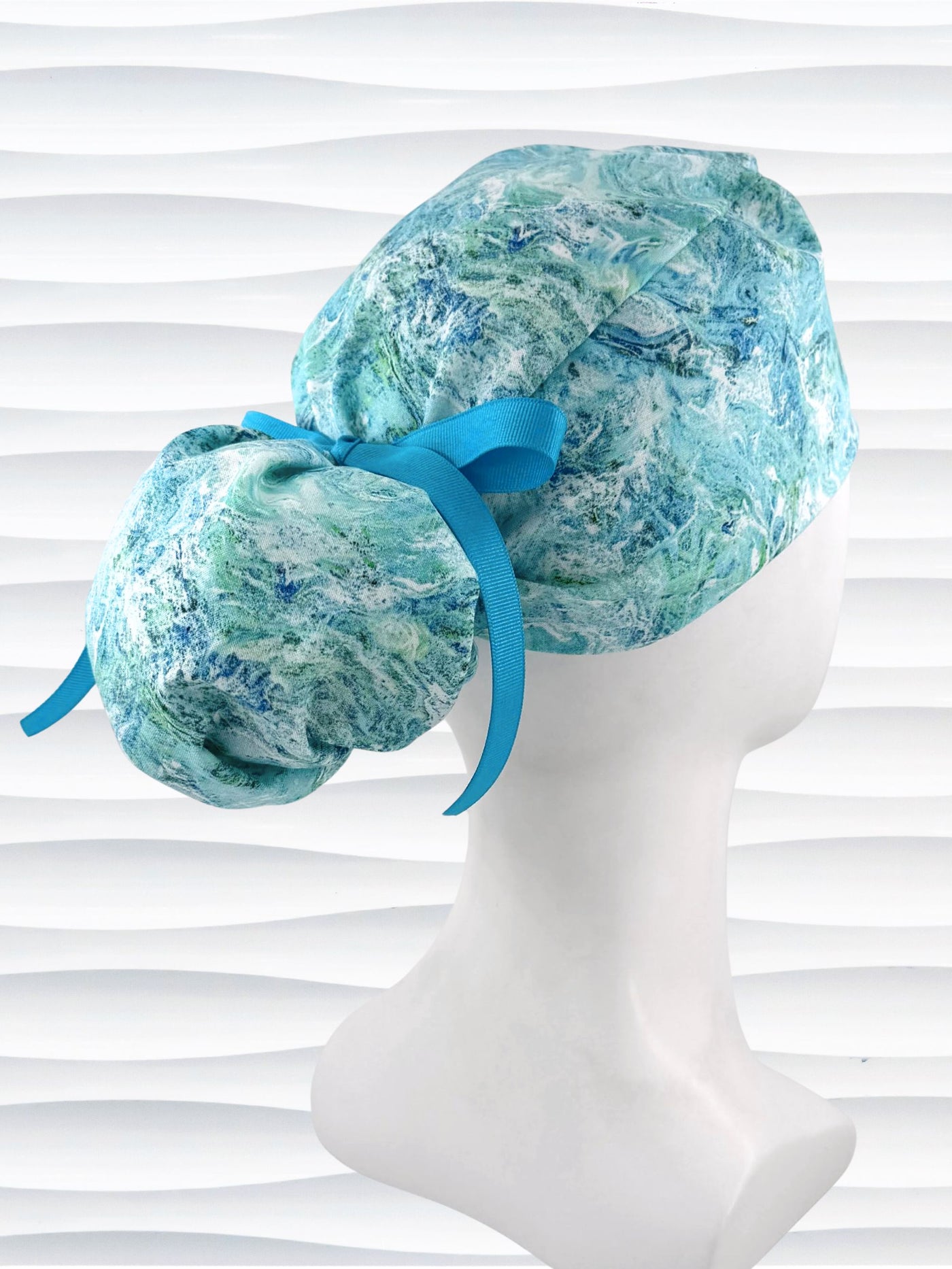 Ponytail style surgical scrub cap by JensCaps with abstract greens and blues on white cotton fabric and displayed on mannequin head.