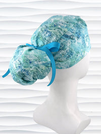 Ponytail style surgical scrub cap by JensCaps with abstract greens and blues on white cotton fabric and displayed on mannequin head.