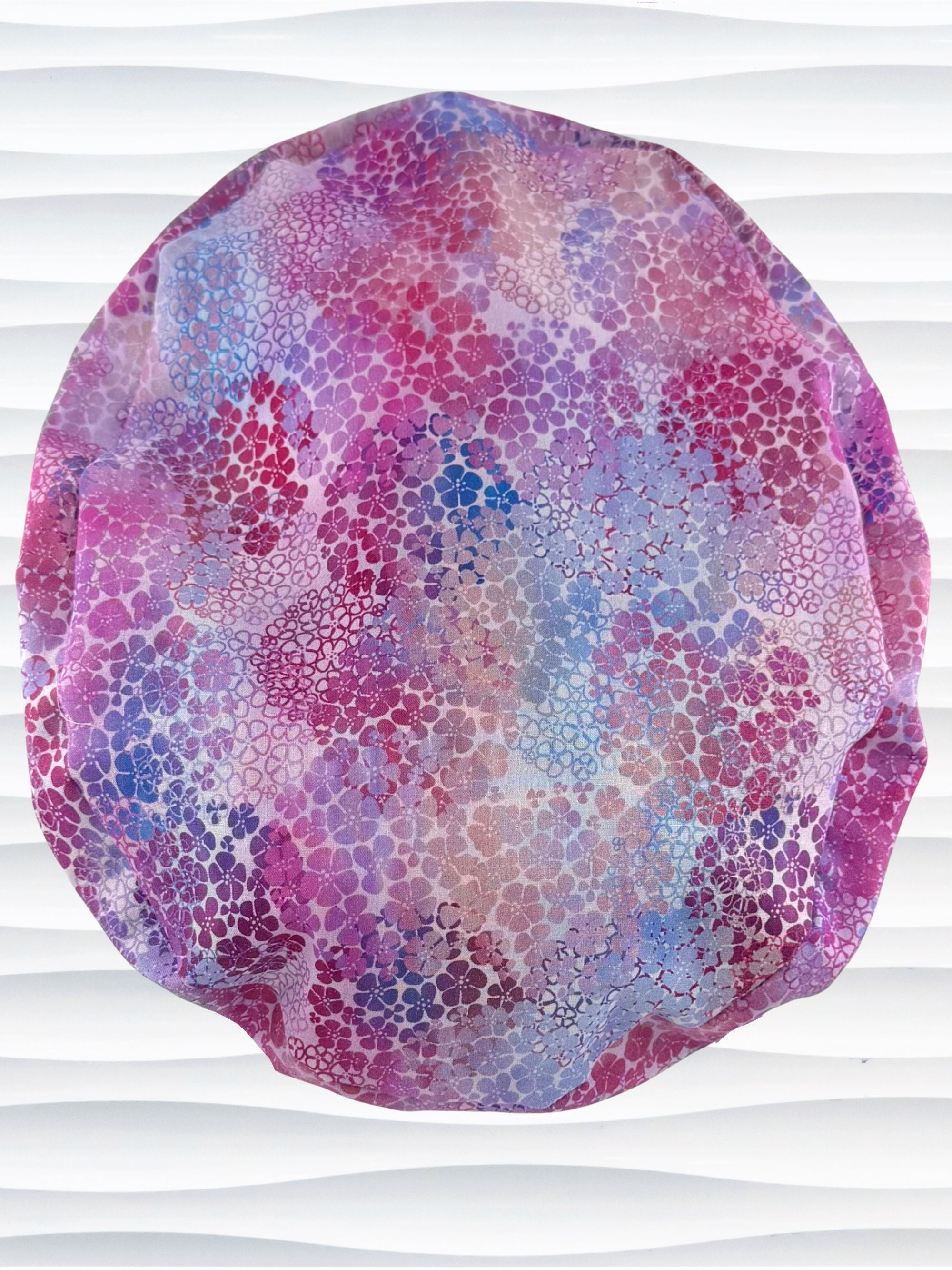 Euro Pony style surgical scrub cap by JensCaps with small daisies in pink, blue, and purple all over cotton fabric and displayed on a mannequin head