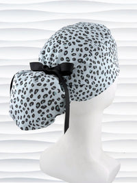 Ponytail style surgical scrub cap by JensCaps with a leopard print on light teal cotton fabric, tied with a ribbon, and displayed on a mannequin head.